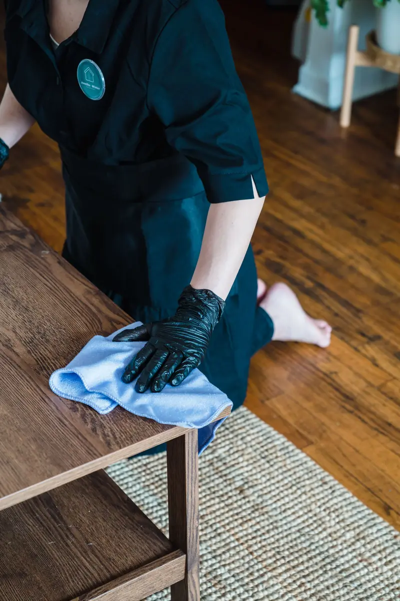 Cleaner in gloves wiping down a wooden table surface